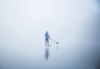 unrecognizable female with paddle on the sup board on the river surrounded of dense fog