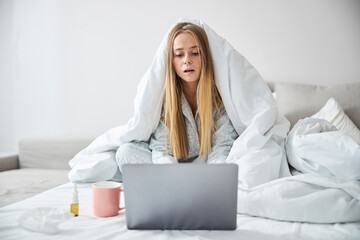 Charming young woman with flu using laptop at home