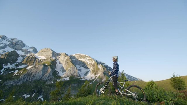 Mountain biker stops to look at abrupt hill from a ridge at sunrise