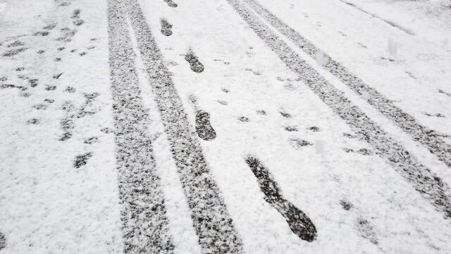 Footprints and tyre tracks on a fresh snow on a road. Snowflakes falling