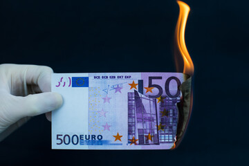 A five hundred euro bill is burning on a black background. World crisis concept.