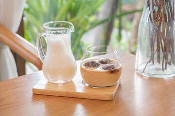 A glass of three iced coffee balls on wood tray served with milk,  homemade latte refreshment in cafe background.