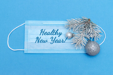 Medical protective mask decorated with a spruce branch and silver balls on a blue background.The inscription of a HEALTHY NEW YEAR! New Year,Christmas and coronavirus concept.
