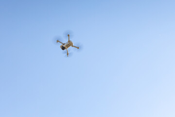 White unmanned aerial vehicle with four propellers and blades is in the blue sky background