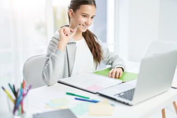 Obraz premium Online class. Cheerful latin teenage girl smiling, looking at the laptop screen while communicating with her teacher, having online lesson at home