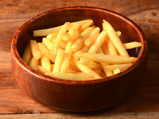 Golden fried French fries served in a wooden bowl over a rustic wooden background, selective focus