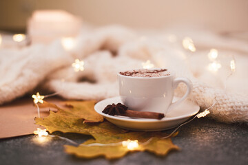 Close up. A cup of hot cappuccino, brown paper, knitted blanket, garland. Copy space.