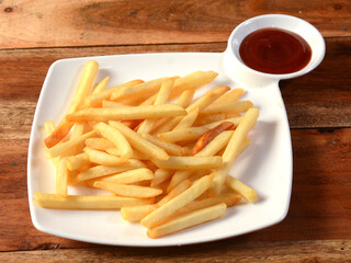 Golden fried French fries served in a plate with tomato ketchup over a rustic wooden background, selective focus