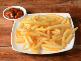 Golden fried French fries served in a plate with tomato ketchup over a rustic wooden background, selective focus