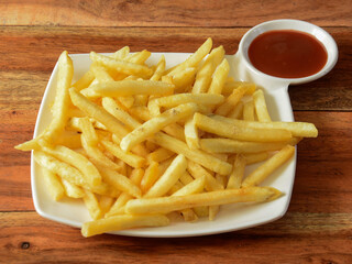 Golden fried French fries served in a plate with tomato ketchup over a rustic wooden background, selective focus