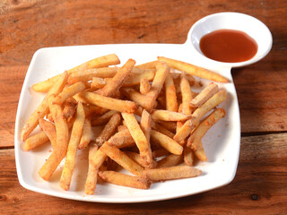 Garlic flavoured French fries served in a plate with tomato ketchup over a rustic wooden background, selective focus