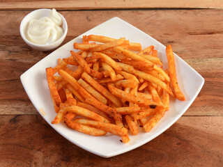 Tasty spicy Peri Peri French Fries with mayonnaise served in a plate over a rustic wooden background, selective focus