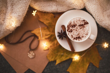 Top view, flat lay. A cup of hot cappuccino with cinnamon. Nearby is a garland, a yellow maple leaf, plaid.