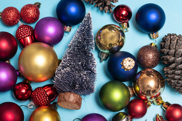 Christmas flat lay with colorful christmas balls, little christmas tree and a pine cone on blue background