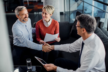 Happy couple handshaking with financial advisor after successful meeting in the office.
