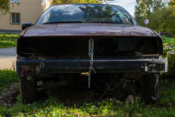 An old car without an engine. The hood is closed with a metal chain with a lock. Front view.