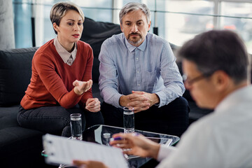 Mid adult couple talking while being on a meeting with insurance agent in the office.