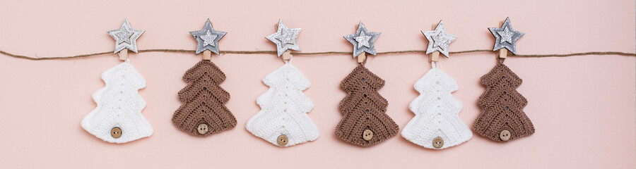 Christmas handmade. Knitted fir-trees in a row on a rope on a pastel background. Handicraft and leisure. Web banner