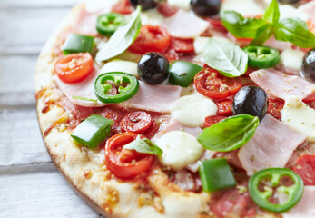 Pizza with ham, mozzarella cheese, cherry tomatoes, green and jalapeno pepper, black olives and fresh basil. Bright background. Close up.	