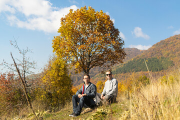 Naklejka na ściany i meble Young men taking a break after long walking in autumn nature