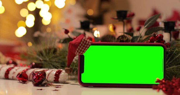 iPhone 12 Pro Max smartphone with pre keyed green screen and Santa Claus' hat on top standing in front of Christmas background. Easy to paste your content.