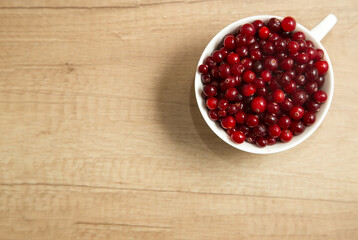 red cranberries in a white cup on a wooden background, flat lay