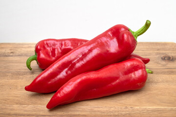 Three red peppers lie on a wooden table