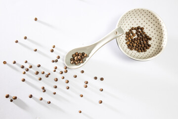 Jamaican Allspice Berries on white with long shadows. Jamaican Allspice Berries in a spoon and a bowl.