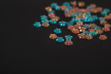 Star-shaped multicolored beads are scattered on a black background. Needlework materials close-up.