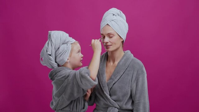 Skillful happy young chilf teenager girl doing pretty makeup for her beautiful mother while having beauty skincare routine in the bathroom. Female beauty. Families.