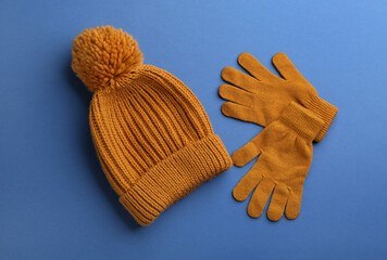 Woolen gloves and hat on blue background, flat lay