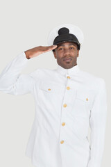 Portrait of confident young African American Navy officer saluting against gray background