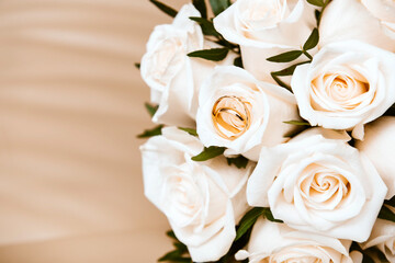 beautiful wedding bouquet of white roses with 2 gold  rings on a beige background