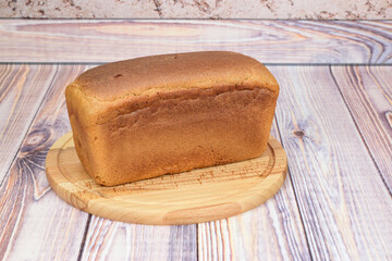 A whole loaf of rye and wheat bread on a wooden cutting board.