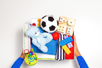 Donation concept. Volunteer hands holding donate box with clothes, books and toys on white background. Top view