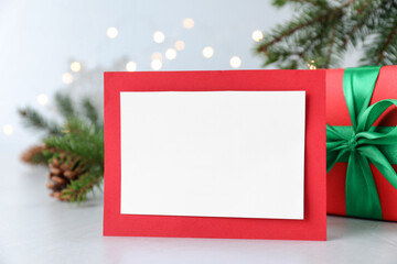 Fototapeta na wymiar Blank Christmas card and gift box on table against blurred fairy lights, closeup. Space for text