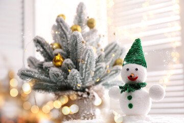 Cute snowman and Christmas decoration near window, bokeh effect. Space for text