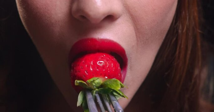 Young woman mouth biting strawberry on a silver fork