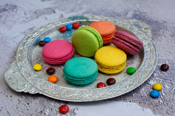 Multi-colored appetizing macarons on a silver platter on a textured background.