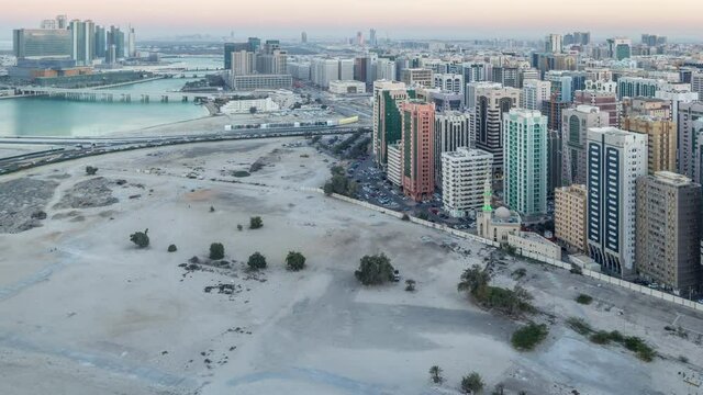 Aerial skyline of Abu Dhabi city centre from above day to night transition timelapse after sunset with illuminated skyscrapers and river.
