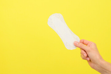 Feminine sanitary napkin in hand on yellow background