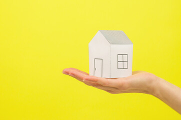 Fototapeta na wymiar Paper house in a female hand on a yellow background. New home buying concept