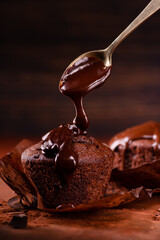 Melted dark chocolate is poured onto a chocolate muffin. dark brown composition and background....