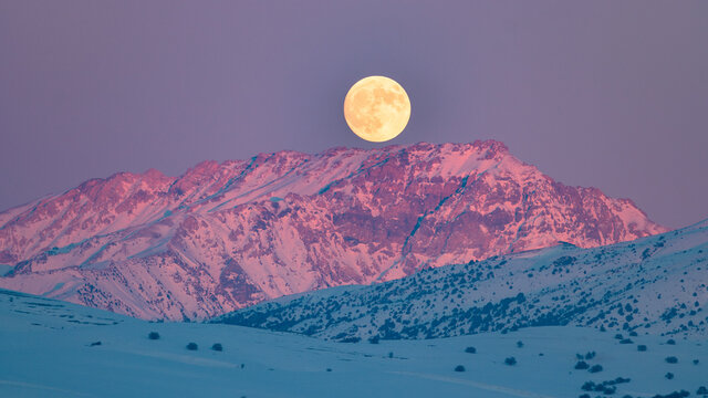 Fantastic orange evening mountain landscape glowing by sunlight. Sunset light with alpen glow and super moon. Full moon rising over a winter mountain landscape.