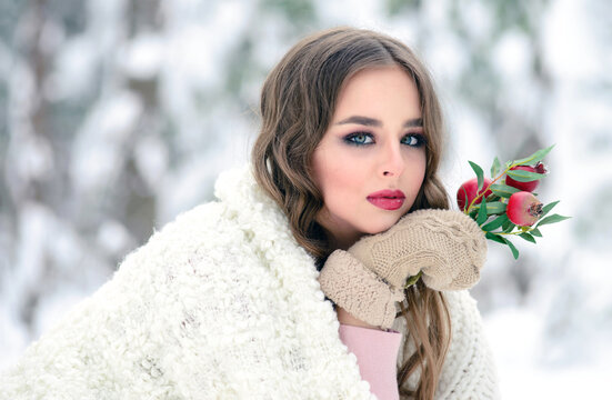 Beautiful young woman with a pomegranate branch. Winter beauty portrait in a snow forest