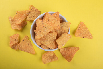 Nachos in a white bowl with yellow background.
