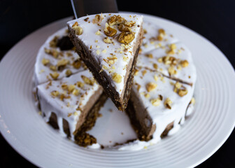 Cut of raw mousse cake with cashew, walnuts and chocolate with white glaze topping. Vegan sugar gluten free dessert