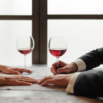 The hands of a young couple dating in a restaurant, there are two glasses of red wine on the table. Valentine day and togetherness concept.