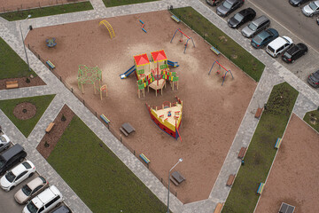Wrong designed yard of an apartment building, dangerous for children with an empty playground and crowded with cars, aerial view.