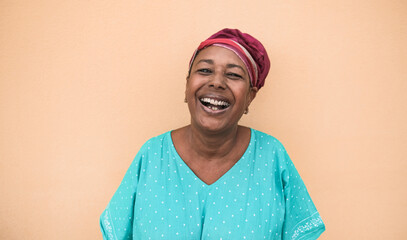 Cheerful african senior woman looking in camera and laughing while wearing traditional dress -...